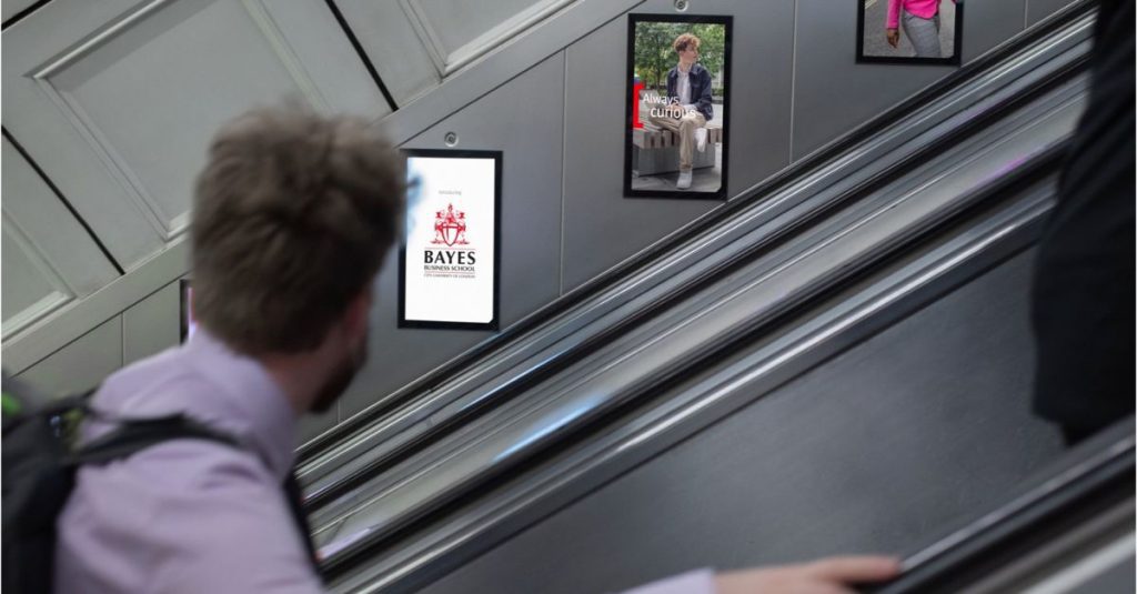 An advert for Bayes Business School displayed using digital escalator panels. A man looks directly at the advert.