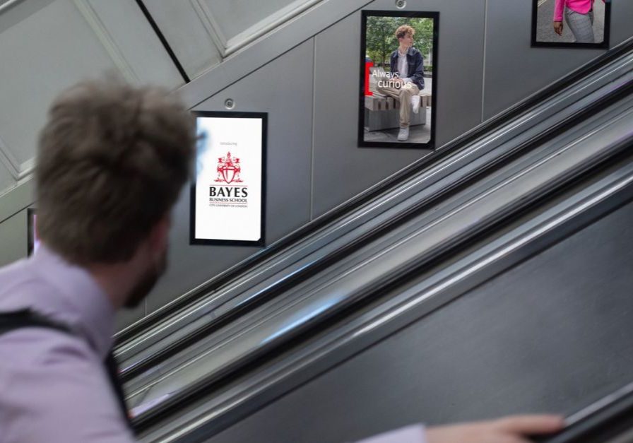 An advert for Bayes Business School displayed using digital escalator panels. A man looks directly at the advert.